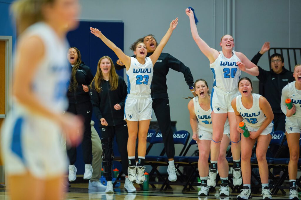 Redshirt freshman guard Mason Oberg (23) cheers on her team from the bench alongside her teammates who are jumping and yelling for their teammates.