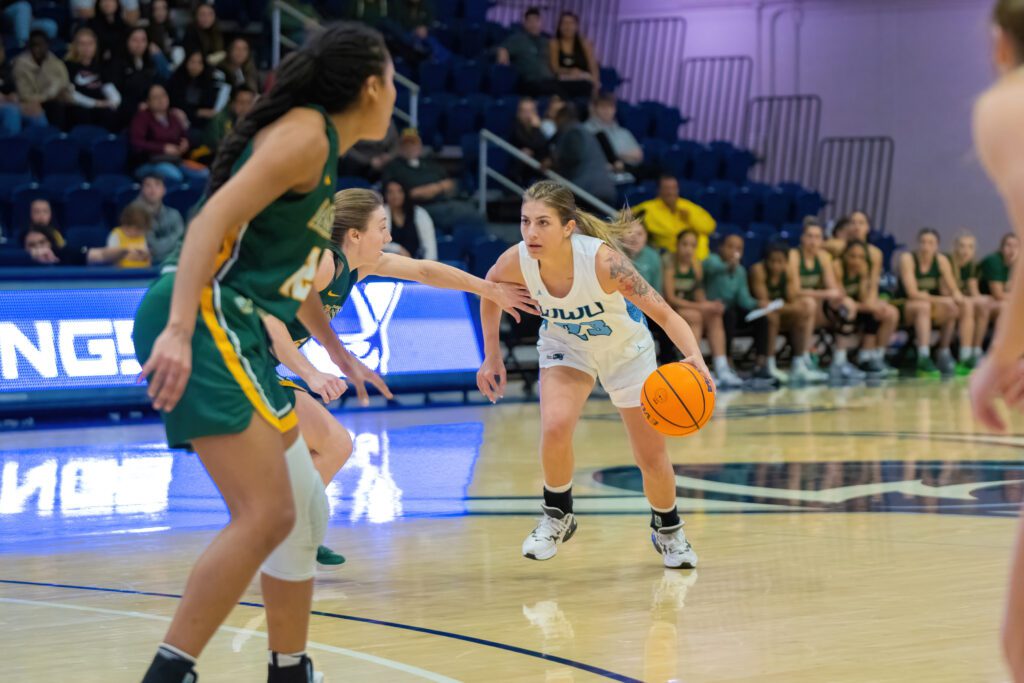 Redshirt freshman guard Mason Oberg dribbles near a pair of Alaska Anchorage defenders as teams and attendees watch closely from the sidelines.