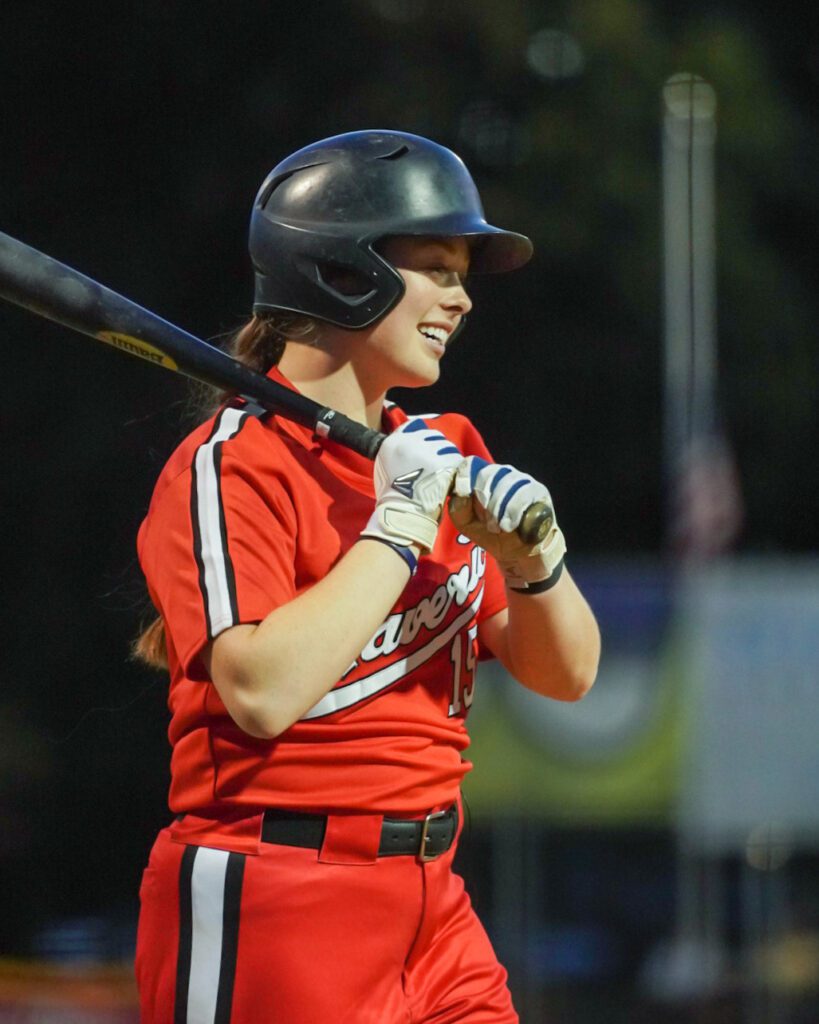 Emily Paulson smiles at the plate with her bat slung over her shoulder.