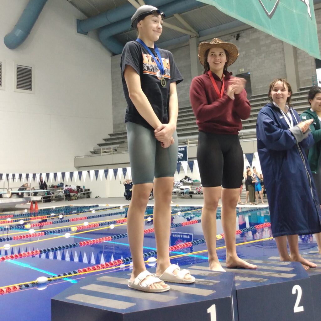 Blaine's Hailey Ferrell is celebrated by other swimmers as she stands on the podium meant for first place.