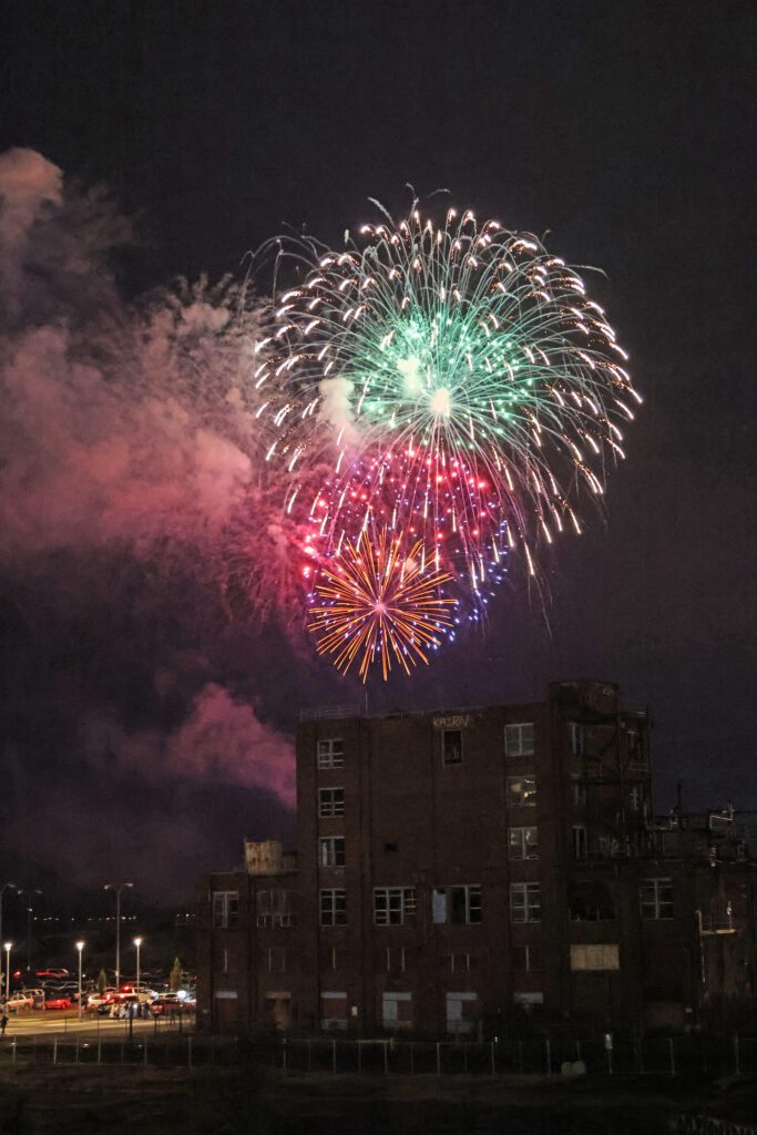 Fireworks of various colors and sizes explode behind the former Georgia-Pacific Alcohol Plant building.