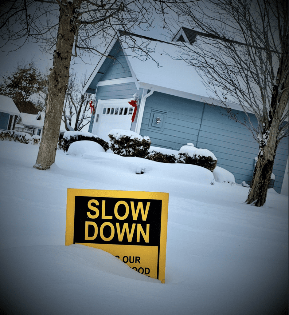 Snow covers a portion of a bright yellow "slow down" sign.