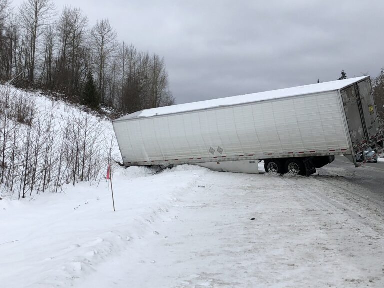 The trailer from a jack-knifed semi truck blocks a lane of Interstate 5 southbound surrounded by snow.