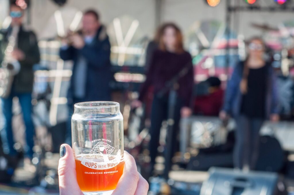 A person holds up a bright orange drink towards the musicians on stage.