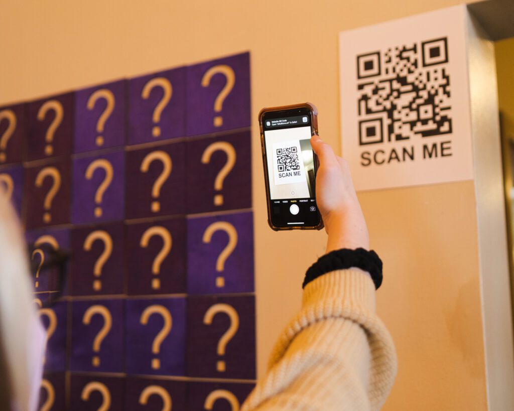 A person holds up their phone to scan the QR code put on the wall.