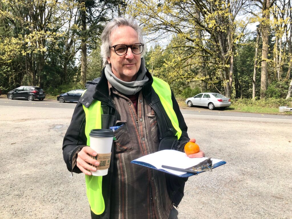 Matt Perry of Fairhaven holding a cup of coffee, an orange, and a clipboard with a pen.