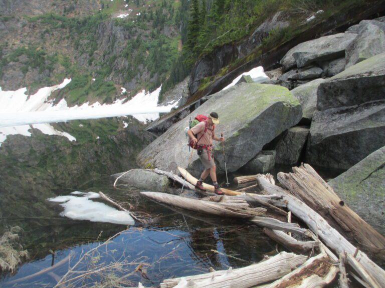 Backpacker Dave Zulinke crosses a log jam with his hiking gear.