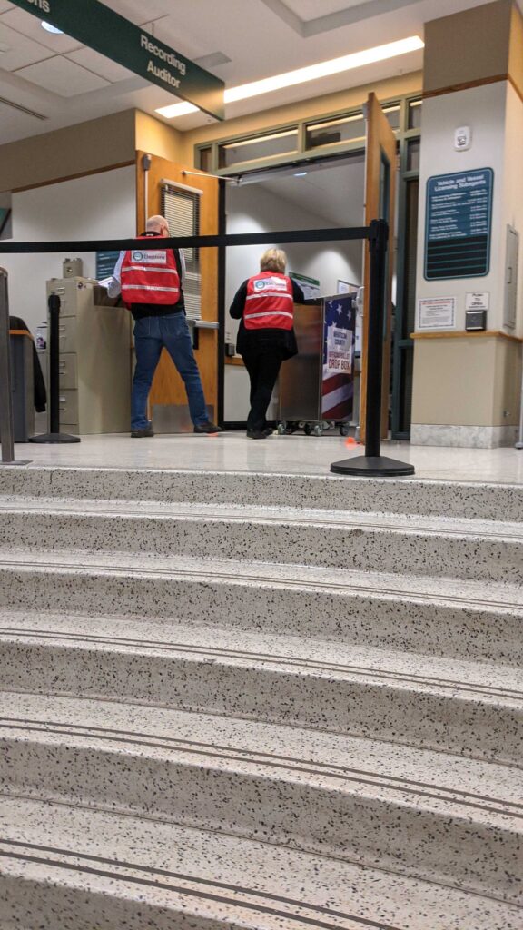 People wheel a ballot box through two open doors.