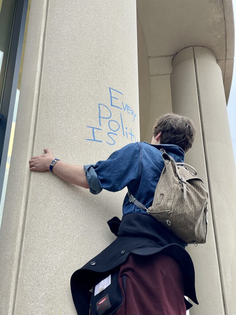 Dylan Petara, a Western Washington student, chalks the Whatcom County Courthouse with the phrase "Every politician is a class traitor," with a blue chalk.