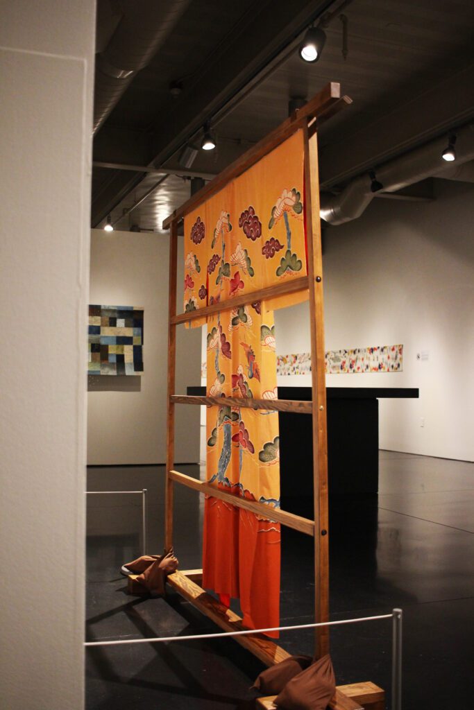 An orange kimono from the '60s by an unknown artist is displayed in a traditional way on a stand the museum.