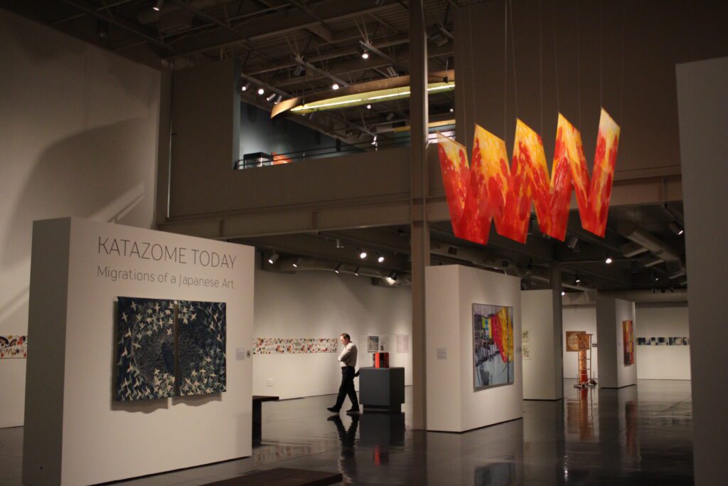 A gallery space with multiple art pieces installed, some with banners hanging from the skies while other pieces are on the walls.