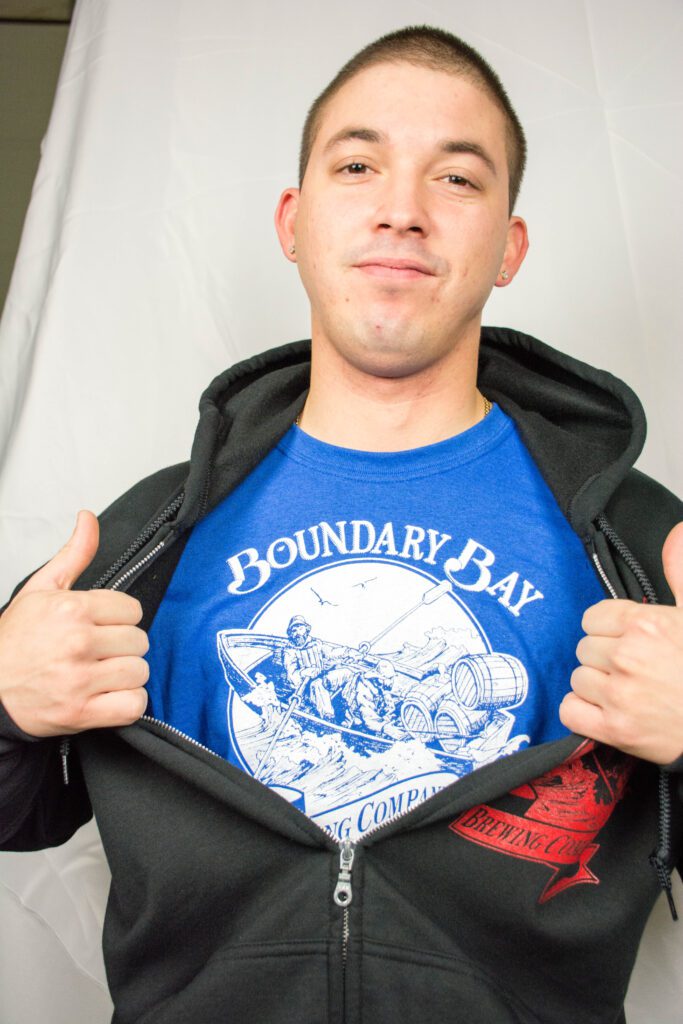 A person opens up their jacket to reveal a bright blue shirt with the Boundary Bay designs printed.