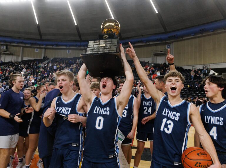 Lynden Christian players celebrate as senior Tyler Sipma (0) holds up the golden trophy with the ball as his teammates cheer all around them.