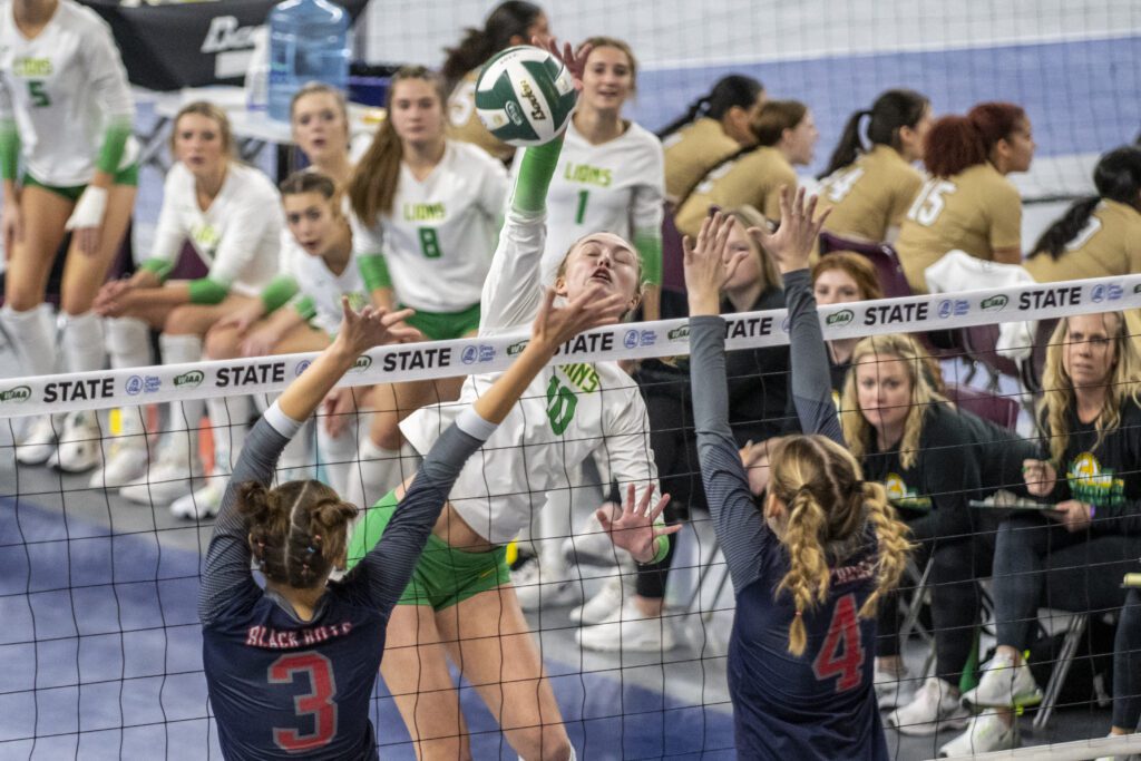 Lynden's Ashley Shumate (10) leaps to spike between two Black Hills blockers with her eyes closed.