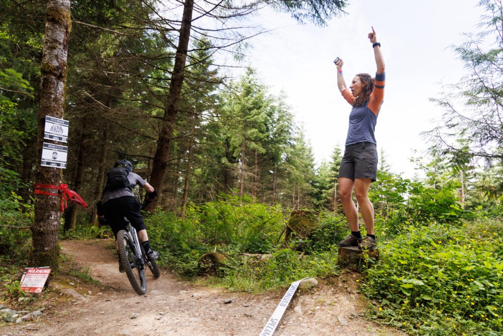 Jade Tabby rings a cowbell on top of a stump as she cheers a biker on.