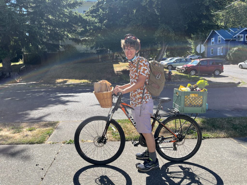 Questen Inghram smiles for the camera while parked on the sidewalk with crates and baskets full of groceries on his E-bike.