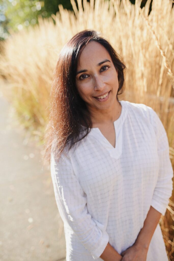 Bellingham-based poet Sati Mookherjee next to tall wheat grass.