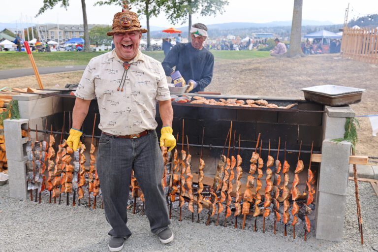 Lummi Nation fish griller Willie Lane reacts with a guffaw in front of rows of grilled seafood as coworkers razz him.