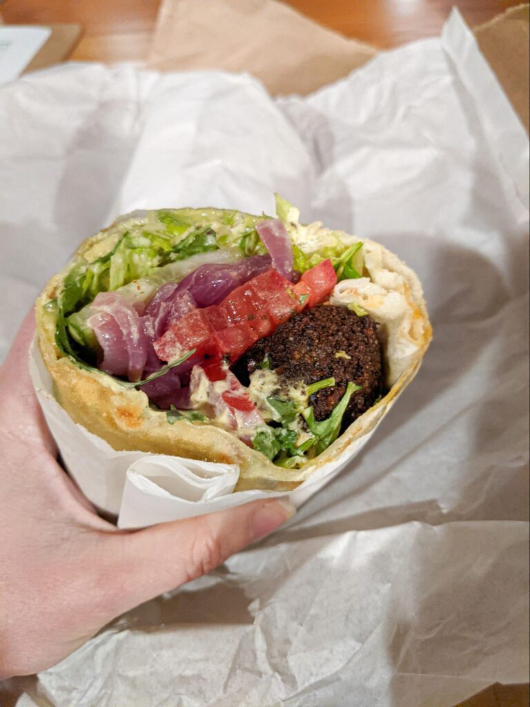 The falafel wrap cross-section shows onions, tomatoes, pickled veggies, and other herbs.