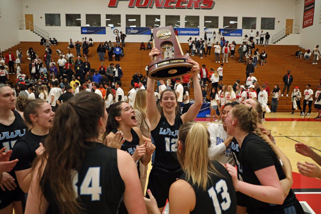 WWU senior guard Emma Duff hoists the NCAA Division II West Region trophy over her cheering teammates.