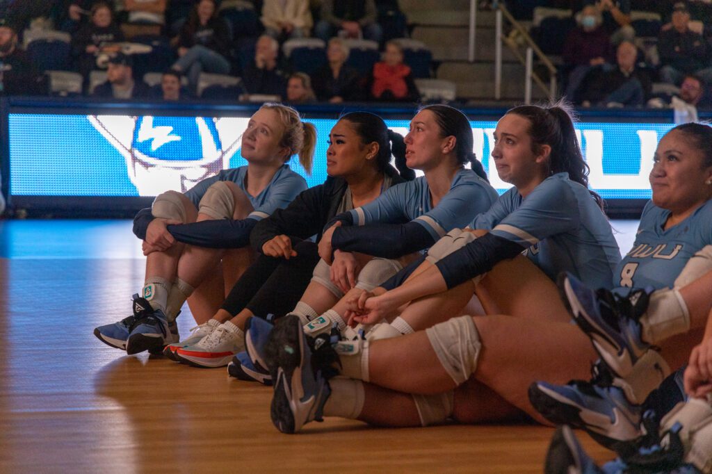 From left, Western Washington University volleyball seniors Olivia Fairchild, Malia Aleaga, Gabby Gunterman, Calley Heilborn and Tupu Lologo sit on the floor of the basketball court as they watch a video commemorating their senior class.