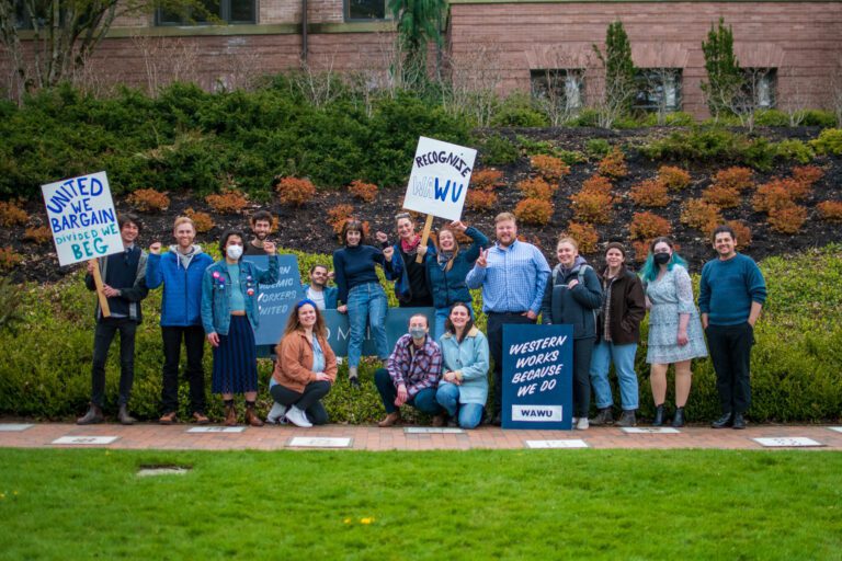 Members of the Western Academic Workers United stand outside Old Main at Western Washington University with various signs.