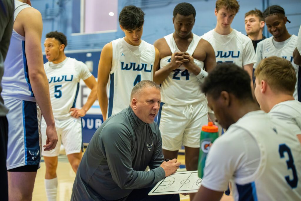 Western head coach Tony Dominguez, kneeling, instructs his team during a timeout.