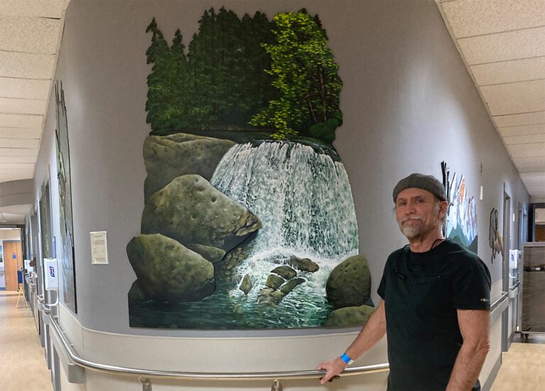 Ron Pattern stands next to one of his paintings that are on permanent display on the third floor of the surgical recovery ward at PeaceHealth St. Joseph Medical Center.