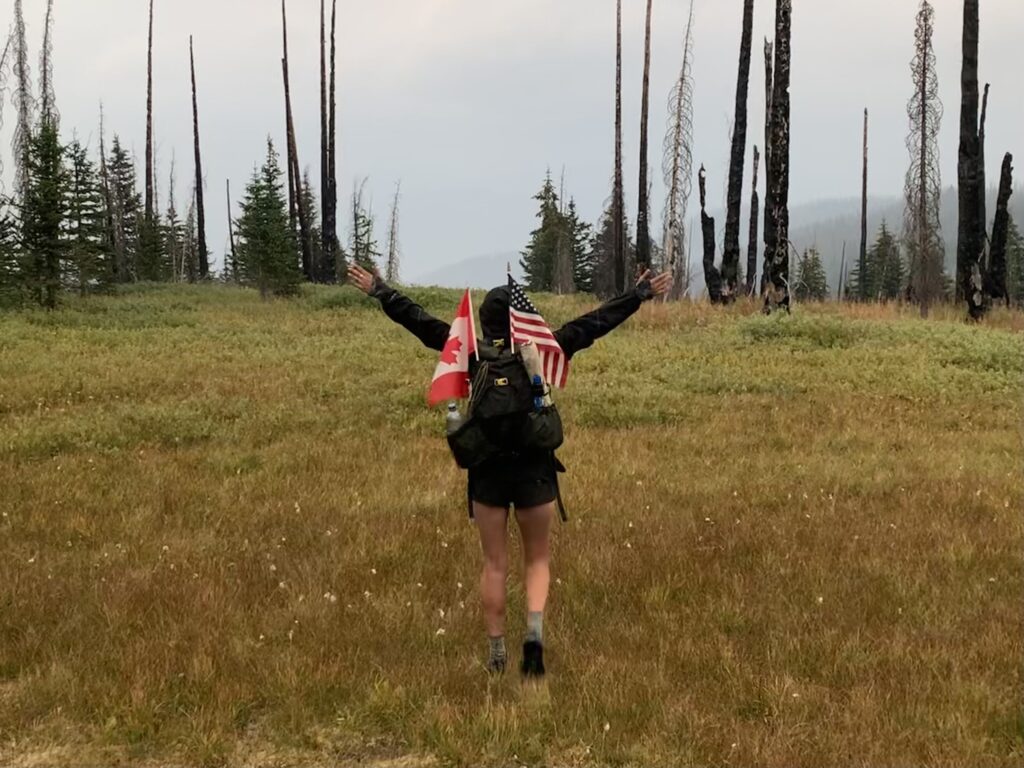 Willow Gebhard of Alger celebrates with arms wide along with American and Canadian flags in their bag.