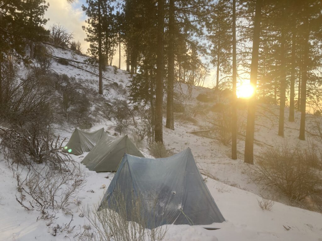 Tents next to each other as the sun rises over the snowy environment.