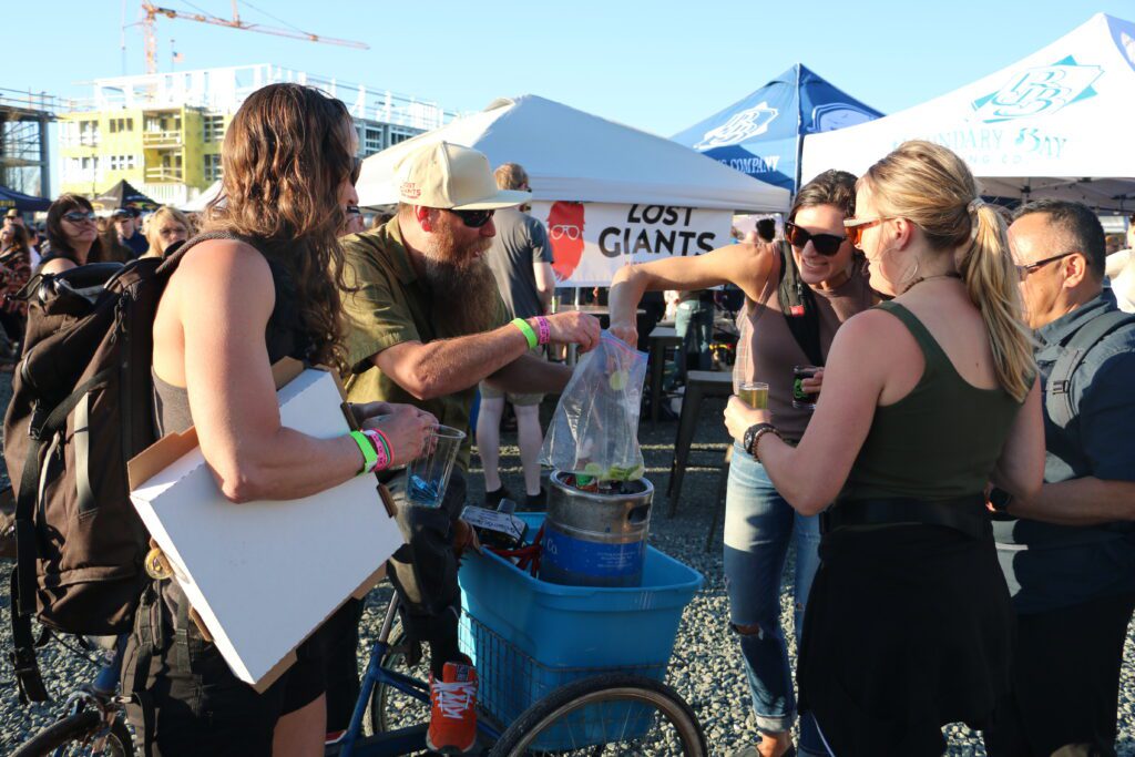 Abe Ebert hands lime slices to an attendee after pouring their glass full of a Boundary Bay beer sampling while others wait for their turn.