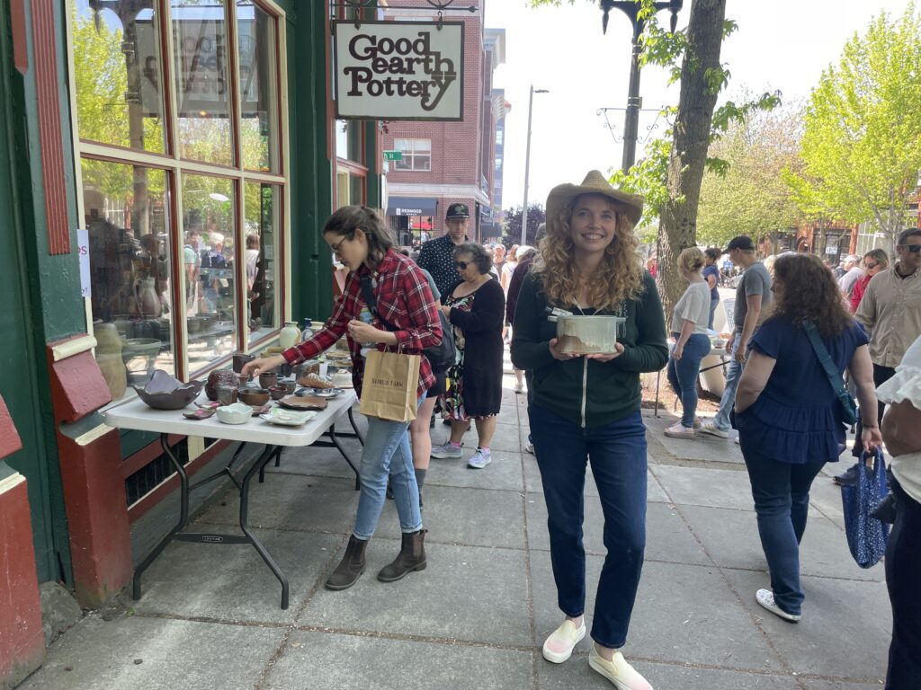 Good Earth Pottery owner and ceramic artist Ann Marie Cooper stands in front of the store with one of her pieces as other attendees browse the rest of her wares.