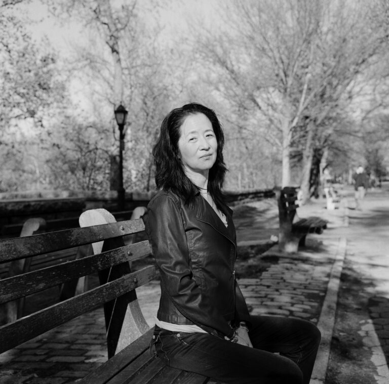 A black and white photo of Julie Otsuka sitting on a bench.