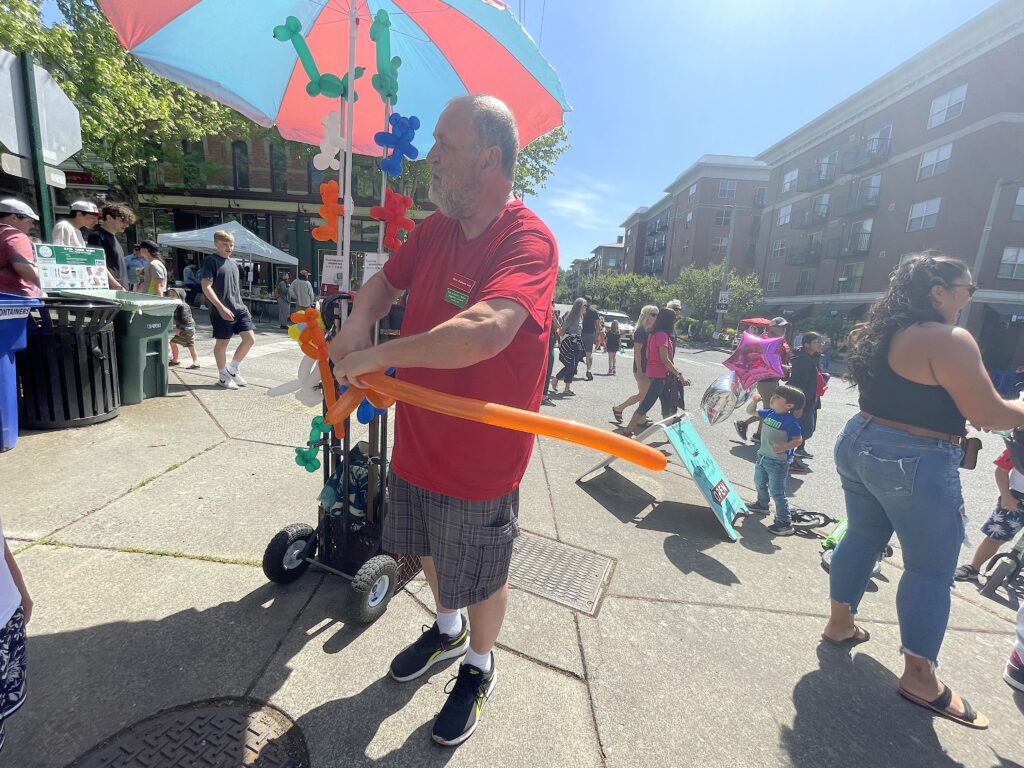 Kevin Pinnell makes a balloon animal with a single orange balloon as kids watch from the side.