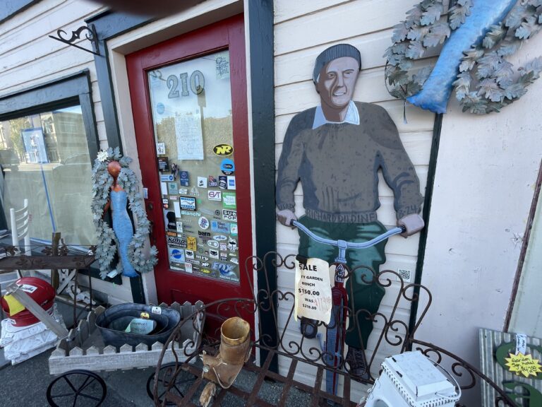 Outside of Alley Cat Antiques in downtown Anacortes, a mural of Richard Dildine and his Ace bicycle is positioned among the wares for sale.