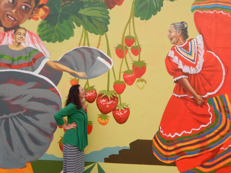 While working on the “Root to Rise” mural commissioned by the City of Burlington, artist Christen Mattix (center) admires her work.