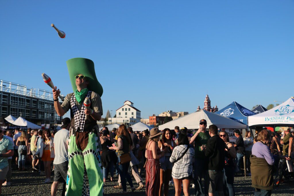 Performer Wren Schultz wearing bright green colors as he towers above the crowd on stilts as he juggles pins.