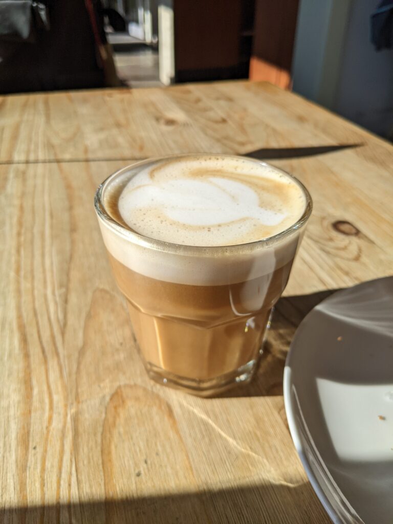 The sun shines on a cup of oat milk cortado.