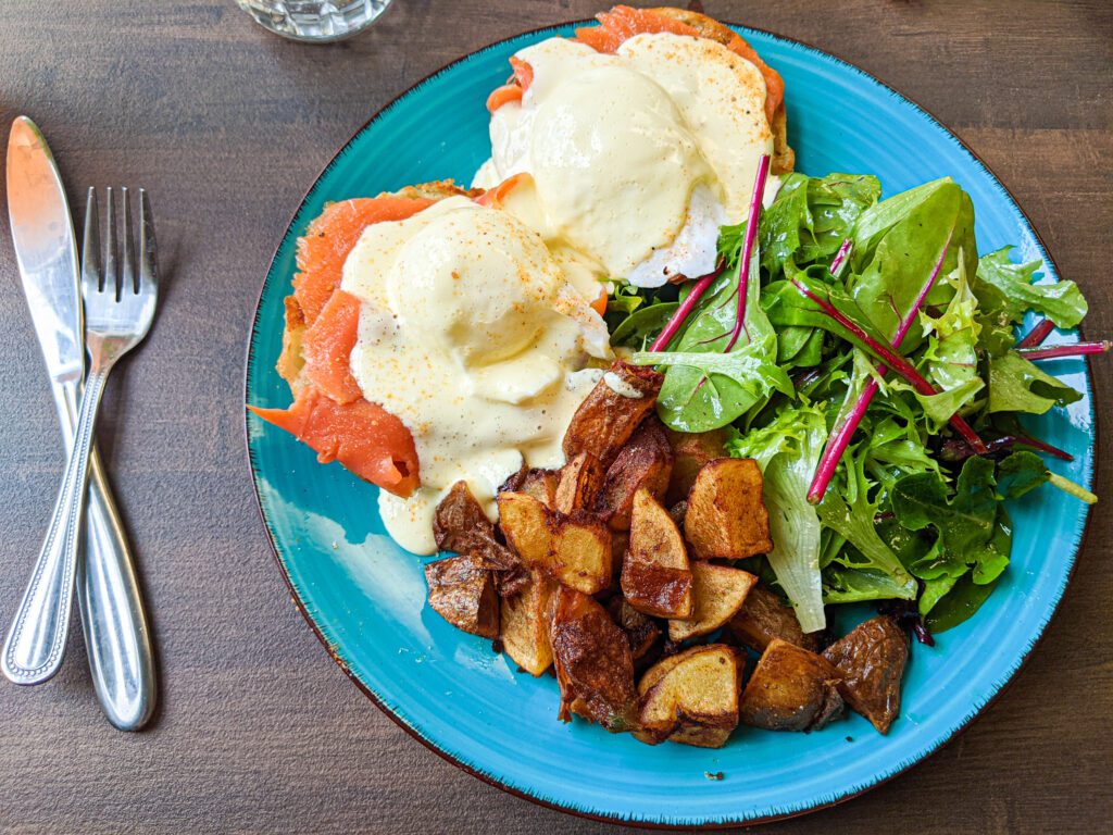 Eggs benedict on smoked salmon are served with a helping of roasted potatoes and a side of dressed salad.