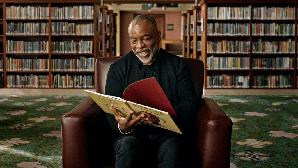 A scene from "Butterfly in the Sky" shows LeVar Burton flipping through a book.