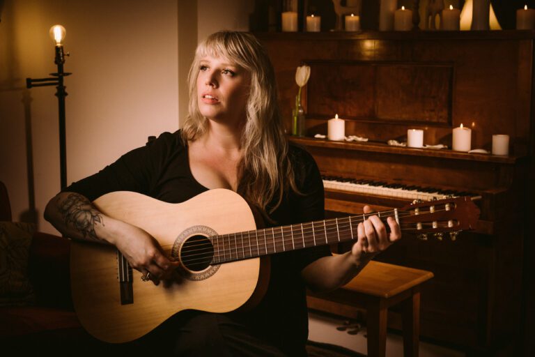 Sarah Goodin holds up an acoustic guitar.