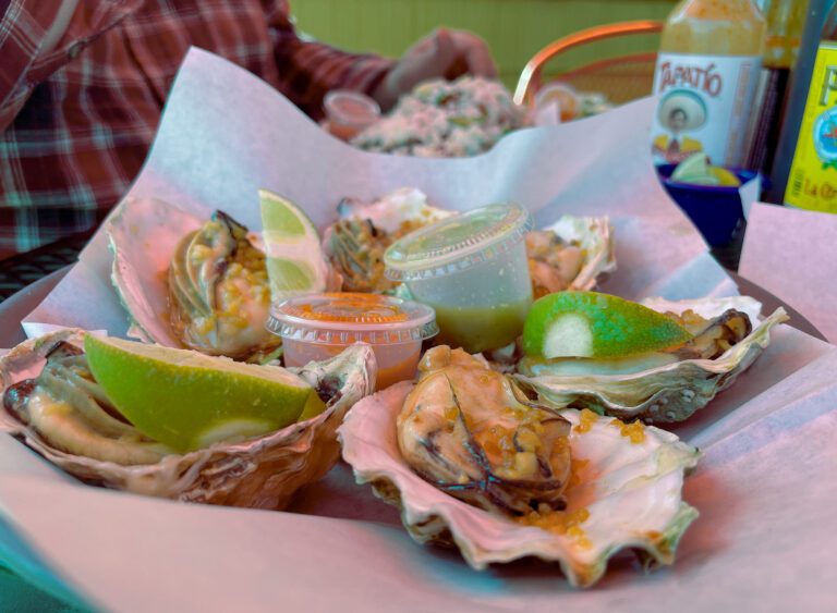 Opened and seasoned oysters topped with sliced lime laid out on a basket with assorted sauces in the center.