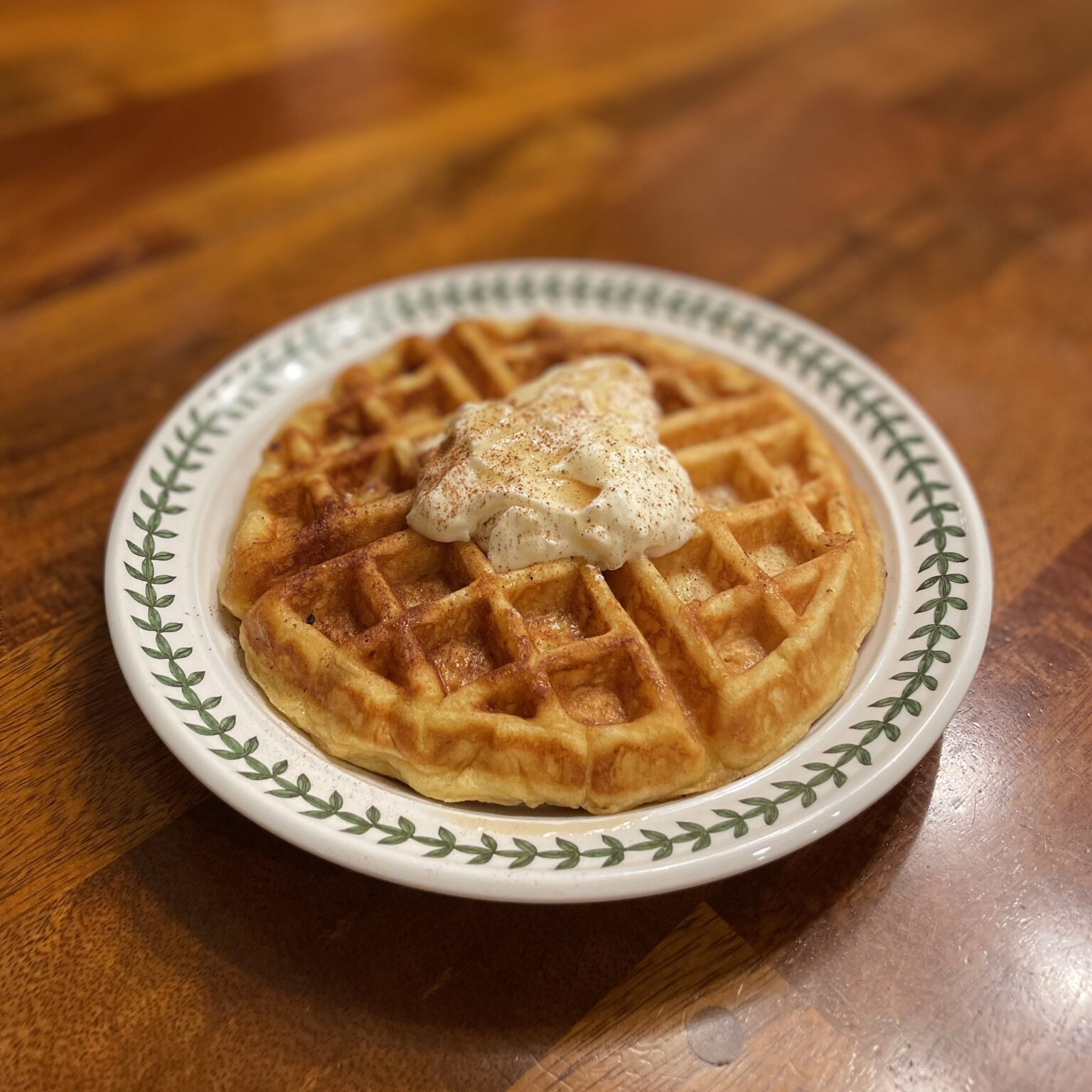 A waffle on a plate with whipped cream.