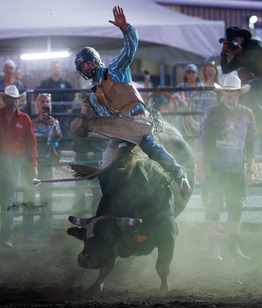 Bull rider Caleb McMillan holds on with one arm in the hand as the bull tries to buck him off.