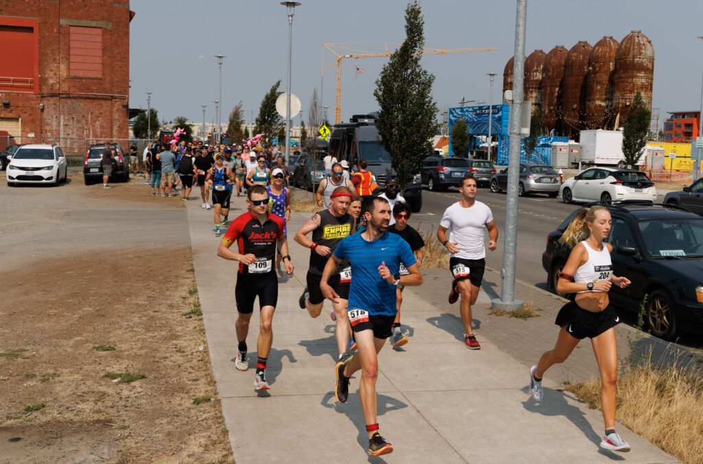 Runners jog along the road on the sidewalk as they leave behind a cheering crowd.