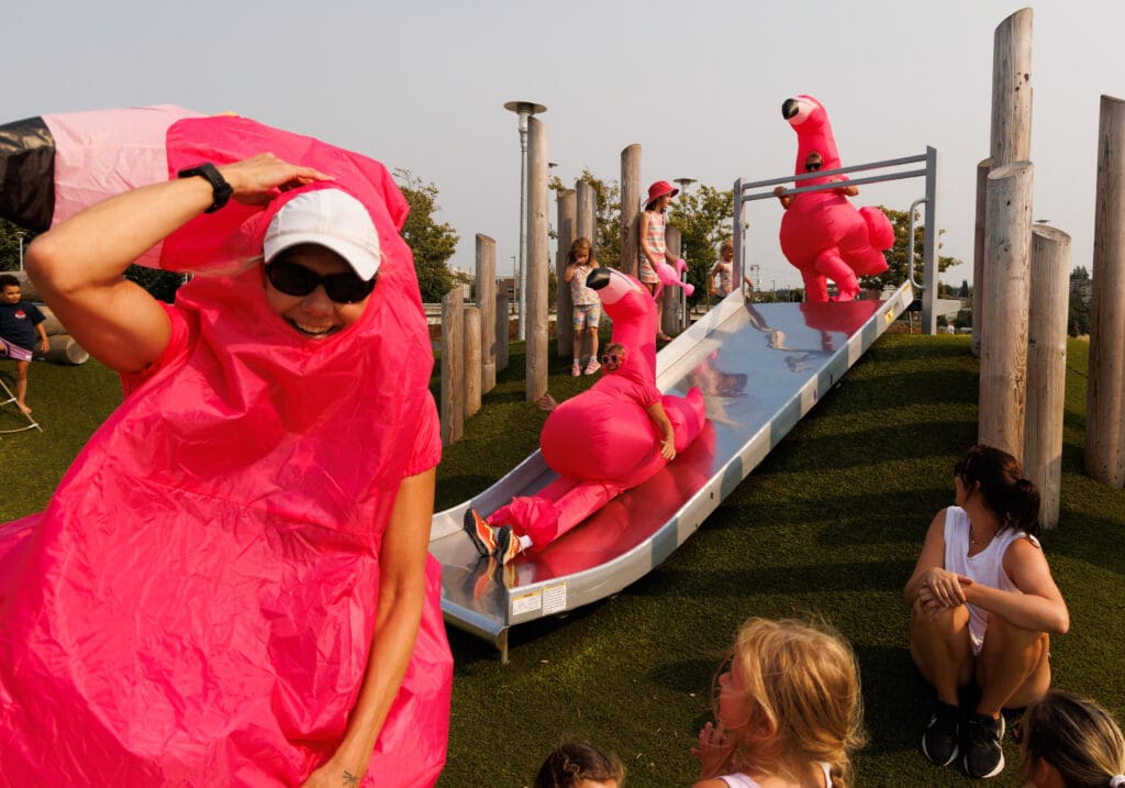 Dressed in inflatable flamingo suits, racers on team YMCA Department of Fun take turns going down the slide at Waypoint Park before heading to the finish line.