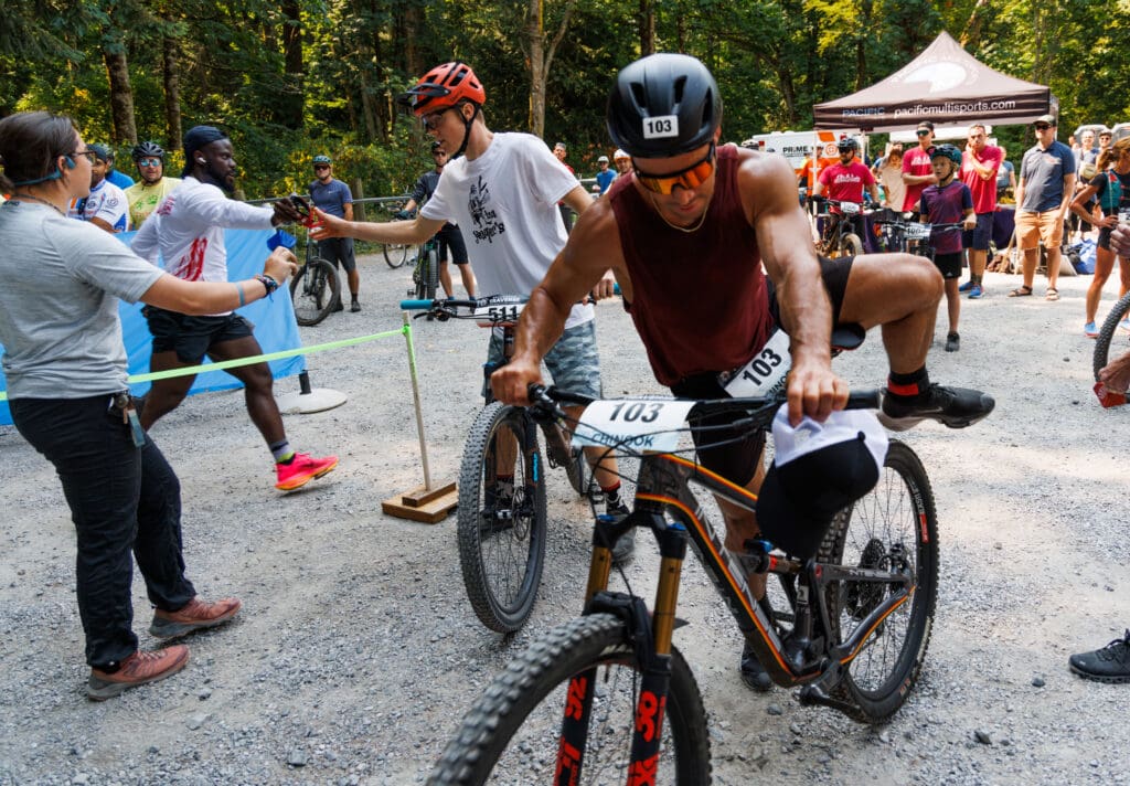 A runner hands off a timing chip to a teammate at the mountain bike exchange at Lake Padden.