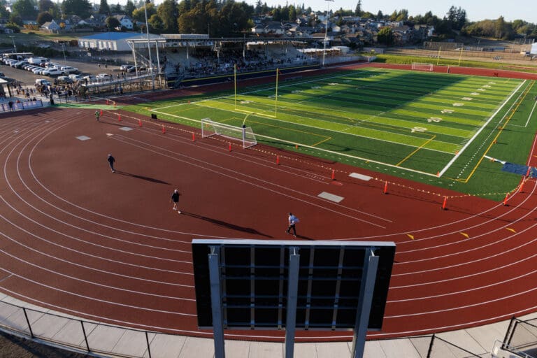 People walk around Ferndale’s new stadium consisting of a large grass field and a red track field next to it.