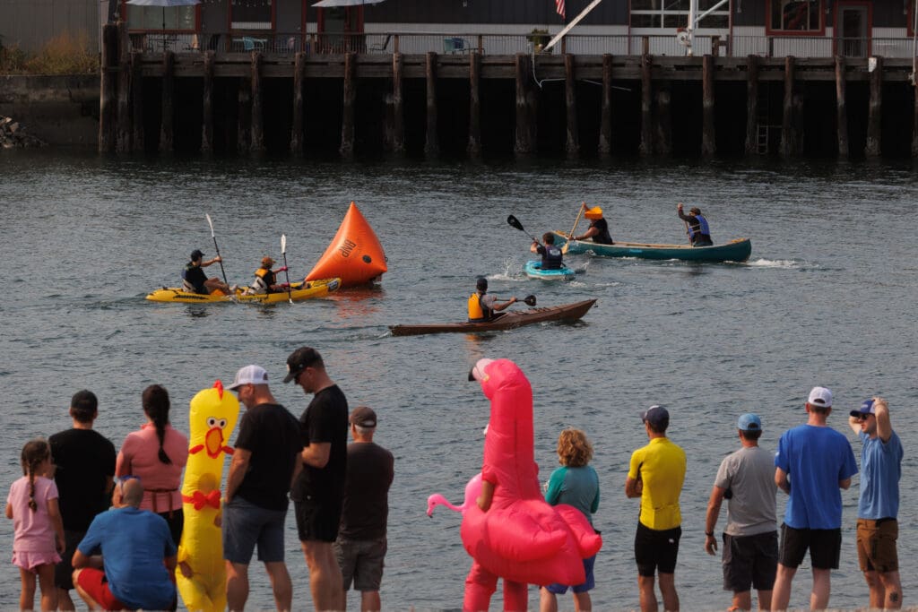 Spectators, with some attendees dressed up as a chicken and flamingo, watch paddlers in Whatcom Creek channel.