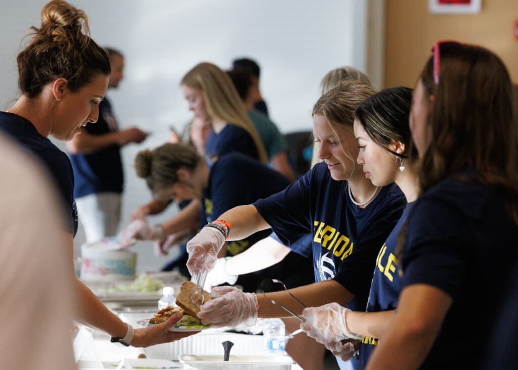 Ferndale volleyball players serve up food wearing plastic gloves as they help a visitor.
